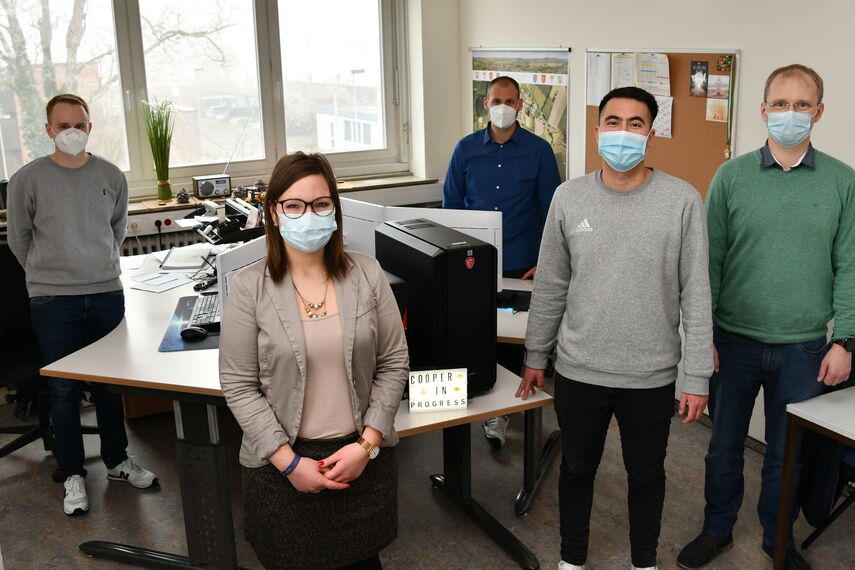 5 Personen stehen mit einer Maske in einem Büro und schauen in die Kamera.